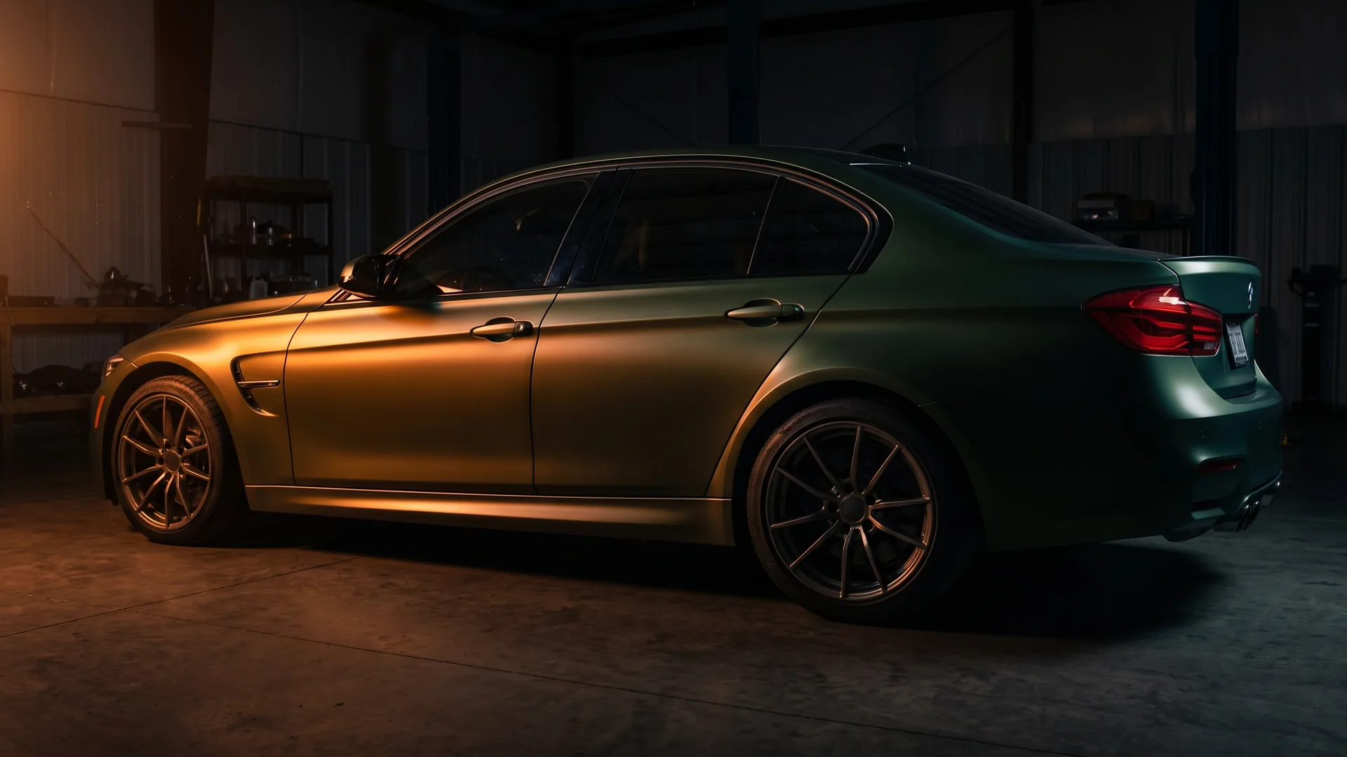 A car finished in a satin green-to-gold colour-shift wrap, seen along its full flank in a workshop. The surface stays matte where paint would flare, so it reads as film rather than a respray.
