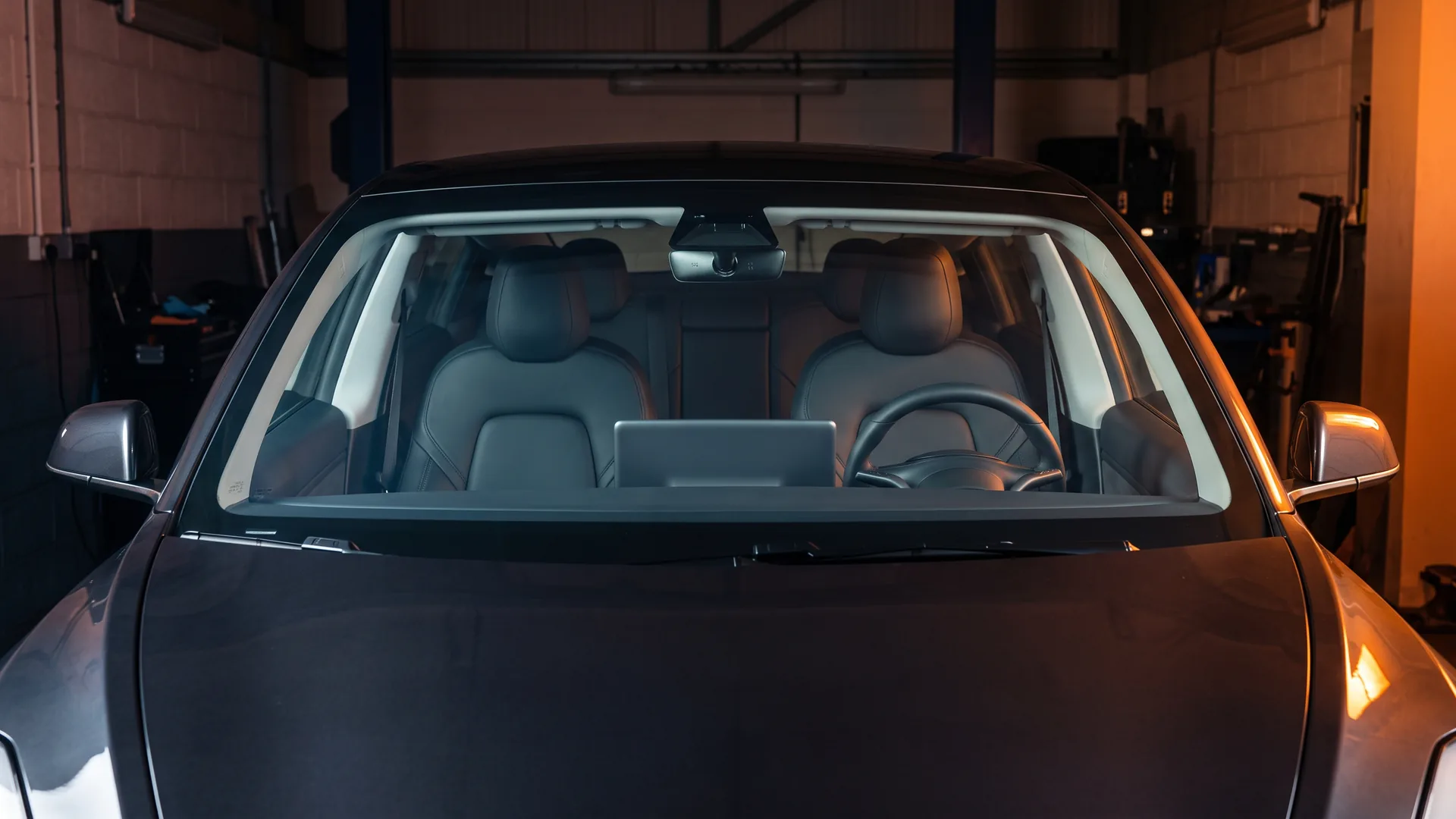 Clear heat-rejection film being worked across the full curve of a car windscreen. The glass stays light and the cabin is plainly visible through it.