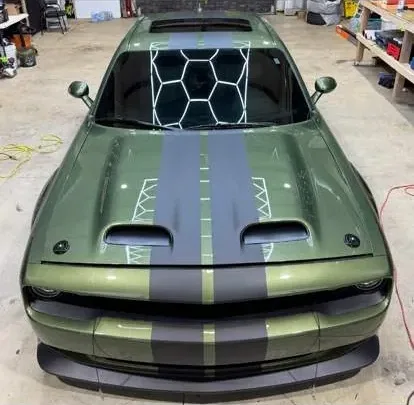 Military green Dodge Challenger with grey centre stripes and a honeycomb pattern banner across the top of the windscreen.