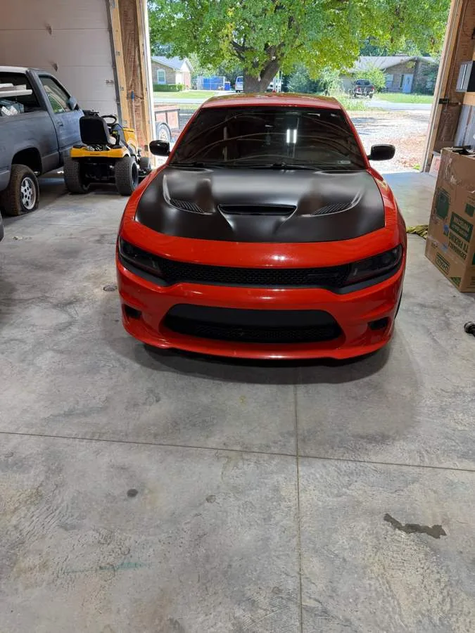 Red Dodge Charger with a satin black wrapped hood and tinted windscreen, photographed head on in the shop.
