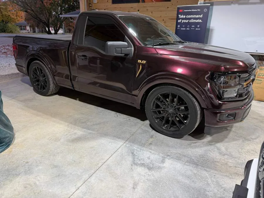 Burgundy Ford F-150 with tinted glass and gloss black wheels inside the shop, a 3M window film display board behind it.
