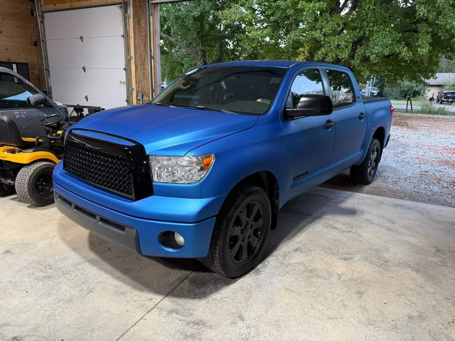 Toyota Tundra wrapped in satin blue vinyl with a blacked-out grille, in the shop doorway.